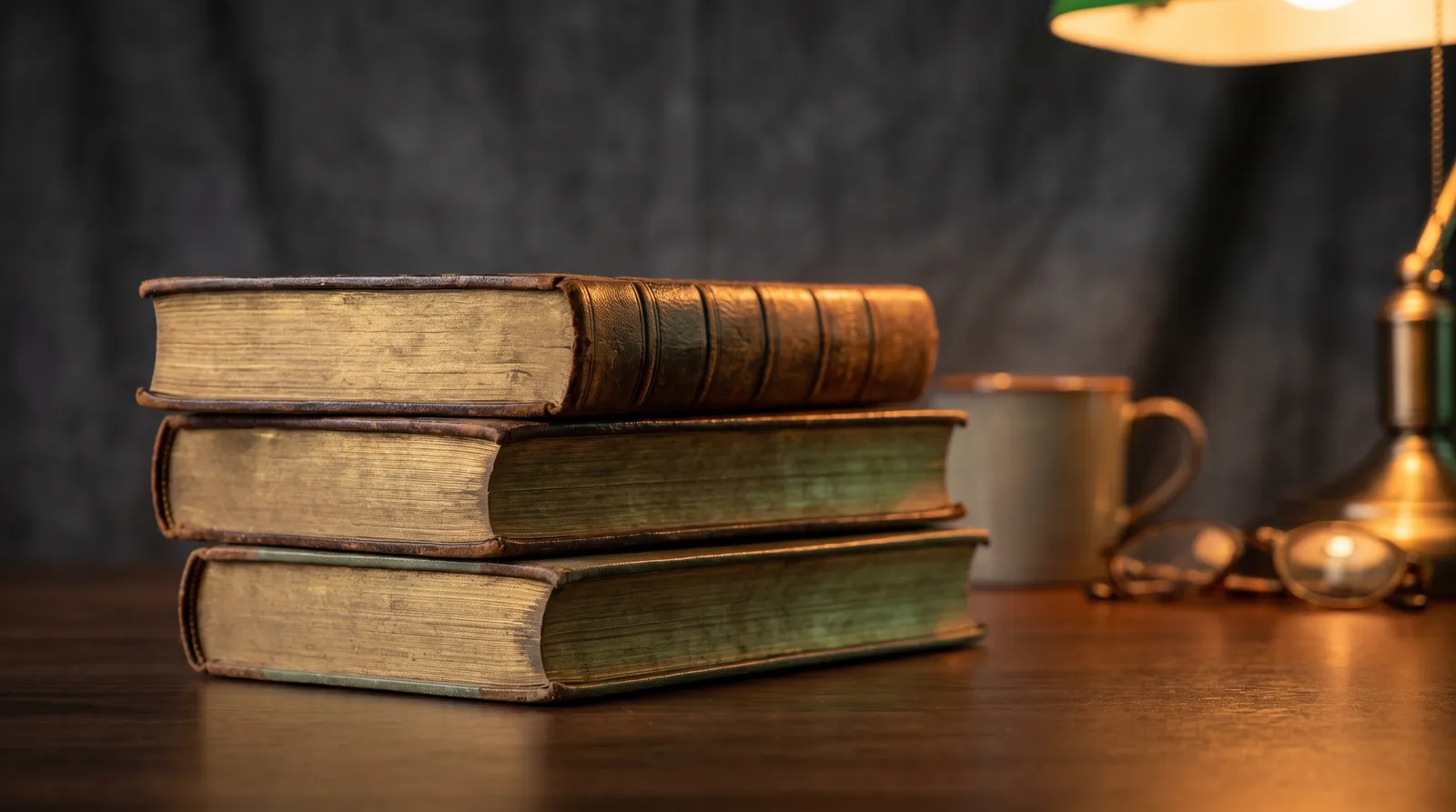 A stack of old leather-bound books with gilded edges under warm scholarly light
